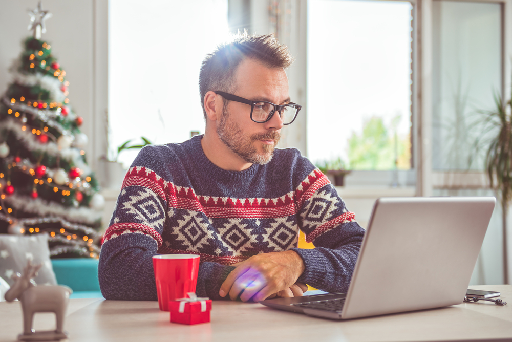 man in a Christmas jumper looking at a laptop with a worried expression